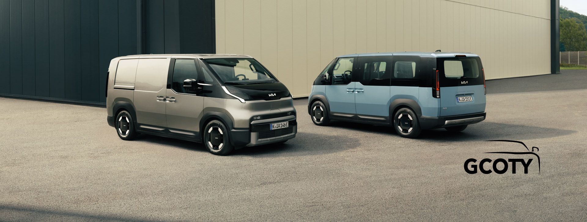 Der Kia PV5 Cargo in schräger Vorderansicht und der Kia PV5 Passenger in schräger Hinteransicht zusammen vor einem gewerblichen Gebäude